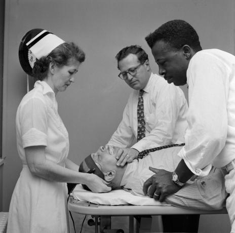 Um médico com atendentes preparando um paciente para terapia eletroconvulsiva.