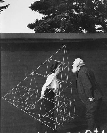 Alexander Graham Bell de frente para sua esposa, Mabel Hubbard Gardiner Bell, que está de pé em uma pipa tetraédrica.