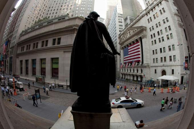 Atrás de uma enorme bandeira americana que cobre a colunata, a fachada da Bolsa de Valores de Nova York é vigiada por uma estátua de George Washington em Wall Street.