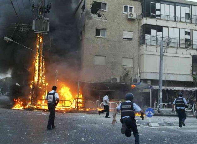 Policiais israelenses correm para o local de um poste de eletricidade em chamas e um prédio danificado momentos depois que uma saraivada de foguetes do Hezbollah atingiu 13 de julho de 2006 na cidade de Nahariya, Israel.