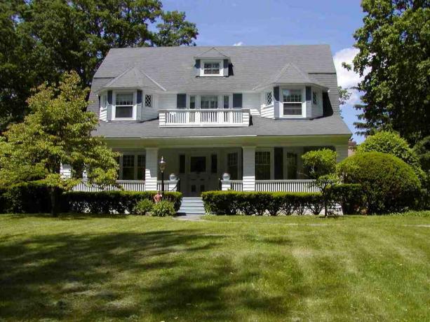 Grande casa branca com enorme telhado cinza frontal e grande gramado verde