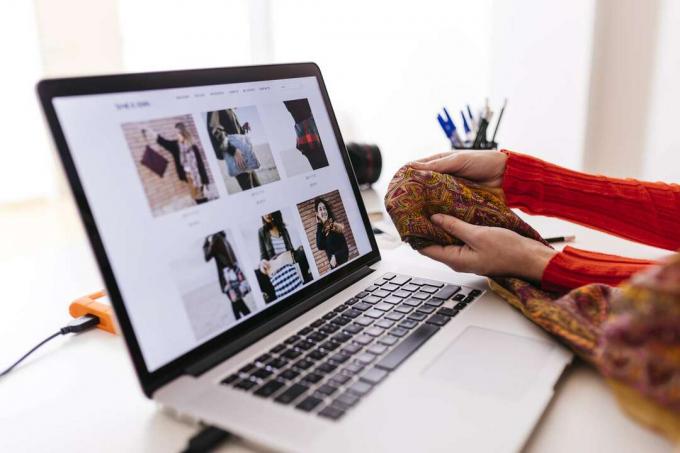 Mulher segurando um tecido na frente de um laptop com um site de moda aberto