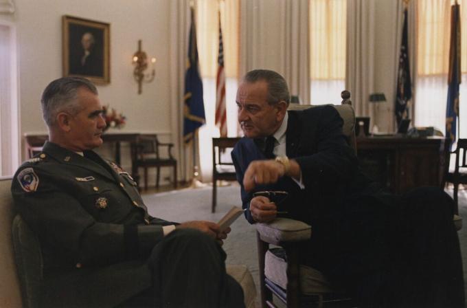 O General William Westmoreland, de uniforme do Exército dos EUA e sentado, fala com o Presidente Lyndon B. Johnson no Salão Oval.