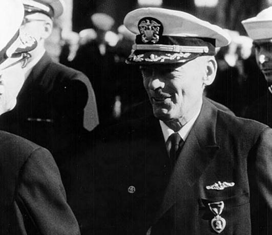 Comandante Lloyd M. Bucher em um uniforme naval recebendo uma medalha.