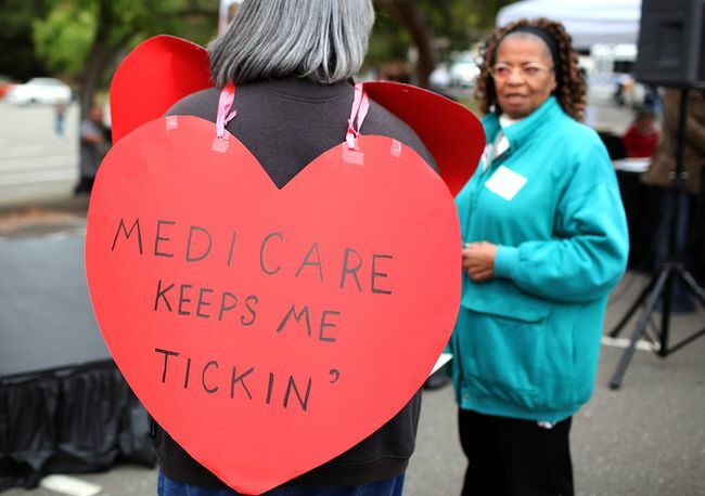 Mulher usando uma placa em forma de coração com os dizeres " Medicare Keeps Me Ticking"