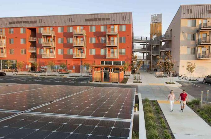 Duas pessoas caminhando perto de edifícios verdes e painéis solares, em uma comunidade Zero Net Energy