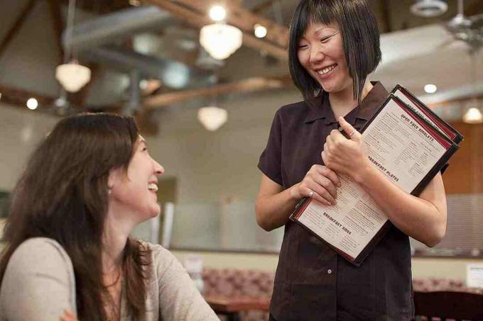 Uma garçonete com menus na mão conversando com um cliente.