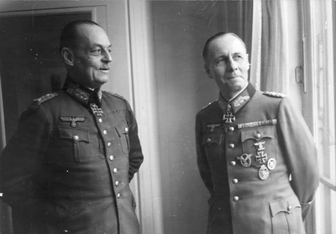 Gerd von Rundstedt e Erwin Rommel em uniformes militares alemães em pé perto de uma janela.