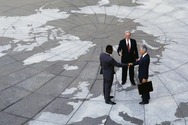  Regionalismo econômico: empresários apertando as mãos no mapa do globo.