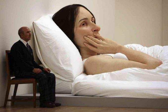 Um homem está sentado ao lado de uma enorme escultura de uma mulher moribunda