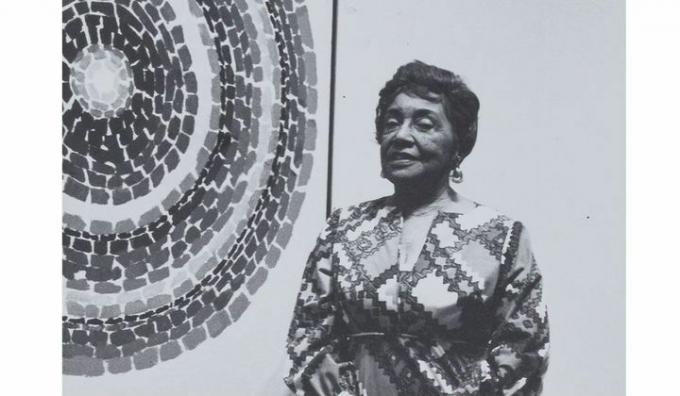 imagem em preto e branco de Alma Thomas na frente de uma de suas abstrações de círculo