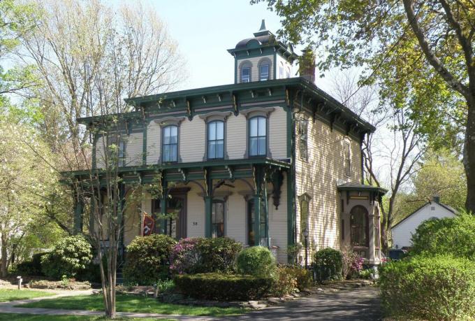 Casa em estilo italiano, 2 andares, tapume amarelado com detalhes em verde e marrom, uma cúpula quadrada em um telhado plano, suportes no teto e alpendre