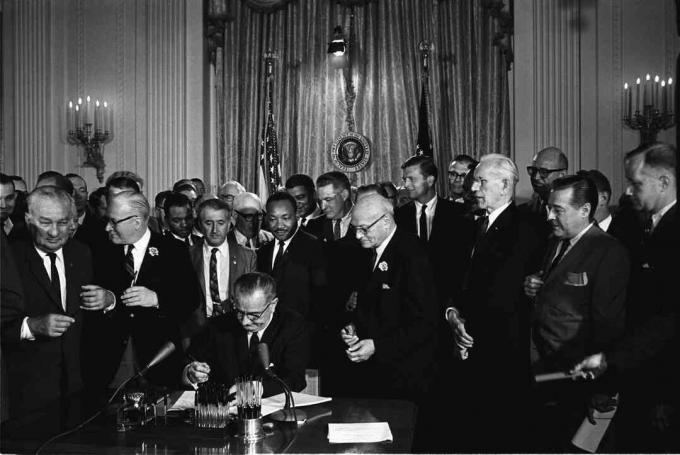 Presidente Lyndon B. Johnson assina a Lei dos Direitos Civis de 1964 enquanto Martin Luther King Jr. e outros observam.