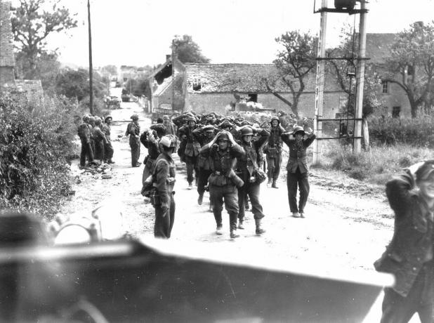 Soldados alemães marchando por uma rua com as mãos na cabeça em sinal de rendição.